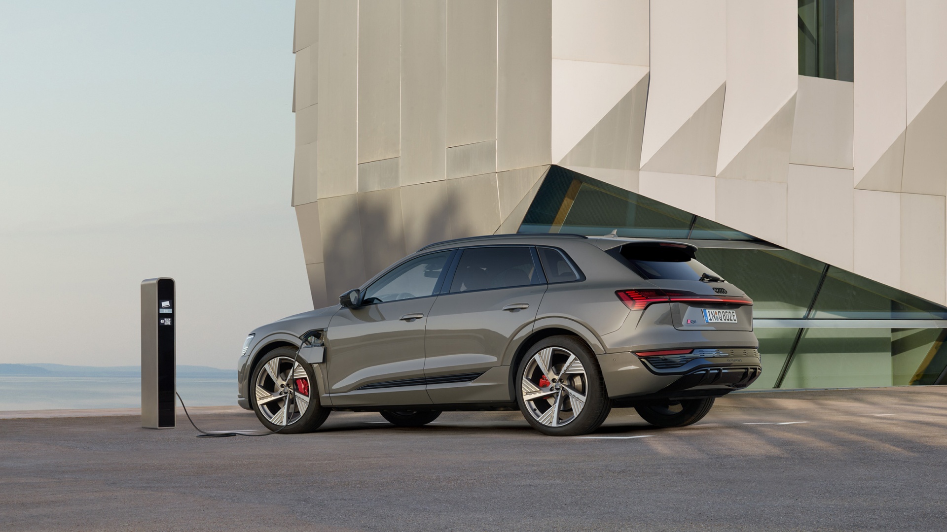 An Audi Q8 e-tron{ft_q8-e-tron} SUV charging in front of a building.